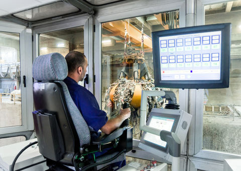 A person operating a crane claw in a waste facility.